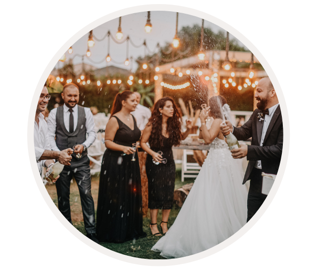 Eine Gruppe von festlich gekleideten Menschen stößt mit Champagner an einer Outdoor-Hochzeitsfeier an, umgeben von Lichterketten.