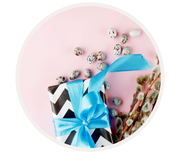 Schwarz-weiß verpacktes Geschenk mit blauem Band, umgeben von Ostereiern und Zweigen auf rosa Oberfläche