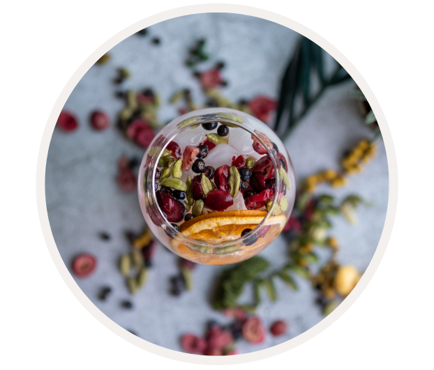 Ein Cocktailglas mit frischen Beeren, Zitrusfrüchten und Kräutern auf einem Tisch, dekorativ angerichtet.