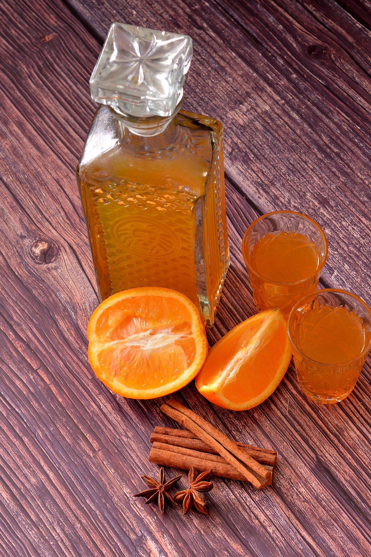 Flasche Orangenlikör mit zwei Gläsern, frischen Orangen, Zimtstangen und Sternanis auf Holztisch