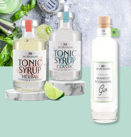 Drei Flaschen: Tonic Sirup Herbal, Tonic Sirup Classic und Mango Rosmarin Gin, dekoriert mit Limetten und Minze