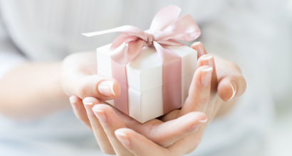Nahaufnahme einer kleinen, weißen Geschenkbox mit rosa Schleife, gehalten von zwei Händen
