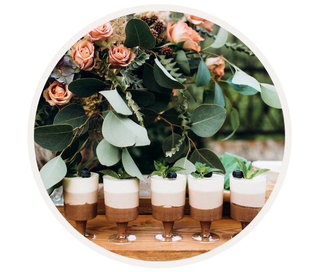 Sechs Gläser mit Schokoladen- und Vanilledessert, dekoriert mit Minzblättern, vor einem Strauß aus Rosen und grünen Blätter