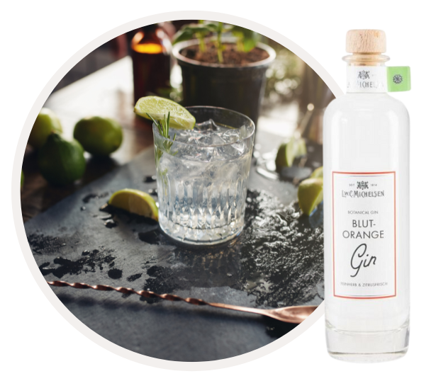 Ein Glas Gin Tonic mit Limettenscheibe und einer Flasche Blut-Orange Gin auf einem Tisch