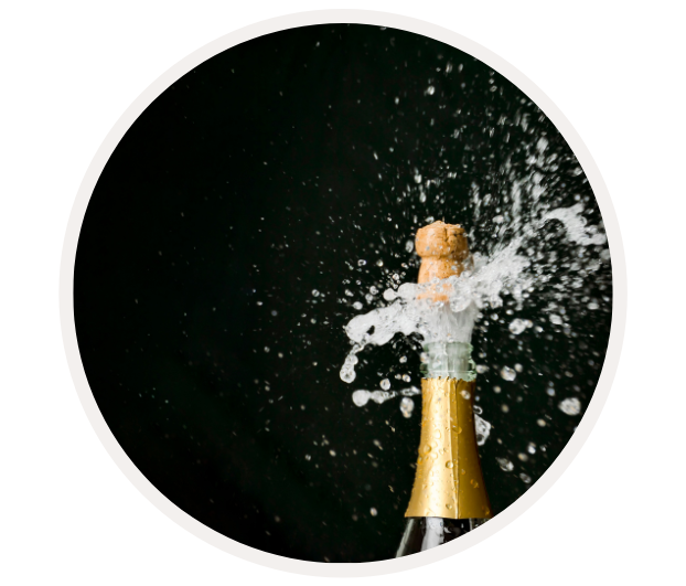 Ein Champagnerkorken schießt aus einer Flasche, umgeben von spritzendem Schaum gegen schwarzen Hintergrund.