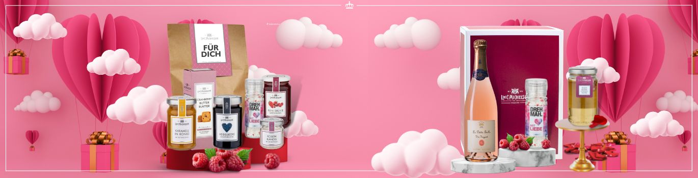 Geschenkset mit Sektflasche, Gewürzen und Delikatessen vor rosa Herz-Dekorationen