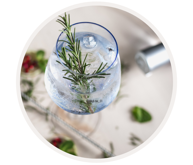 Ein stilvoller Cocktail in einem Glas, garniert mit Rosmarin und Eiswürfeln, mit dezentem Hintergrund und frischen Zutaten