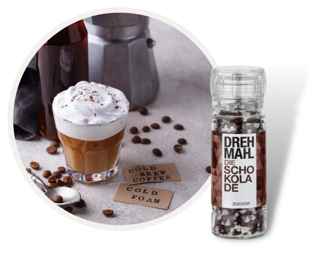 Ein Glas Cold Brew Kaffee mit Schaum neben einer Schokoladen-Zucker-Mühle