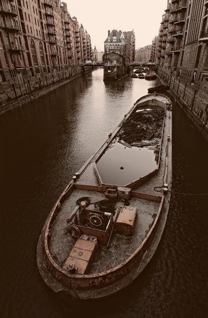 Ein altes Frachtschiff fährt durch einen Kanal der historischen Speicherstadt, umgeben von alten Backsteinhäusern unter einem Abendhimmel.