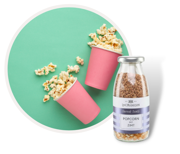 Zwei rosa Becher mit Popcorn und eine Glasflasche mit Zimt-Popcorn vor mintgrünem Hintergrund