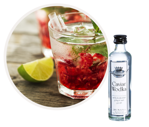 Ein Glas Cocktail aus Caviar Wodka mit Limettenstücken und Himbeeren, daneben eine kleine Flasche Caviar Wodka