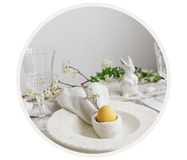 Ein festlich gedeckter Ostertisch mit Glas, Teller, Ei im Stoffhalter und einer dekorativen Hasenfigur im Hintergrund.