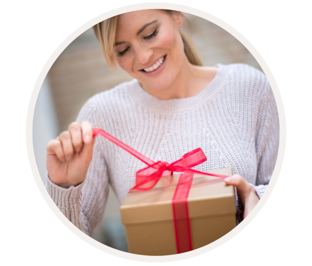 Lächelnde Frau in Strickpullover öffnet freudig ein Geschenk mit rotem Band