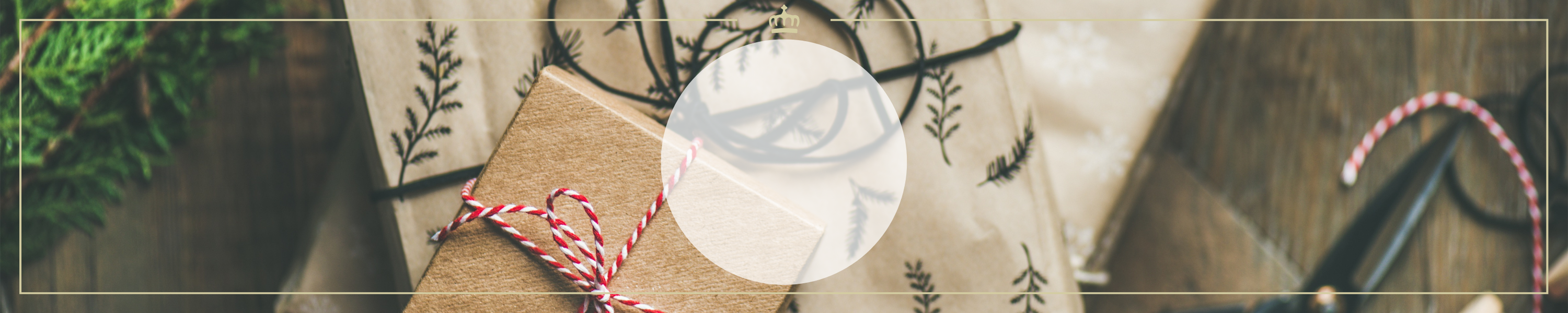Ein weihnachtlich dekoriertes Geschenk mit rotem Band liegt auf einem Holztisch, umgeben von grünem Tannenzweig und Weihnachtsdeko