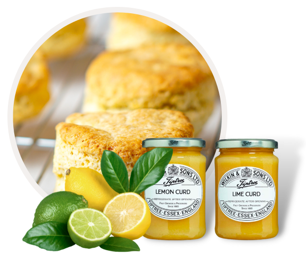 Zwei Gläser Lemon und Lime Curd mit frischen Scones im Hintergrund, umgeben von Zitronen und Limetten
