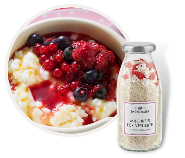 Schale mit Milchreis und roten Beeren neben einer Flasche Milchreis-Mischung