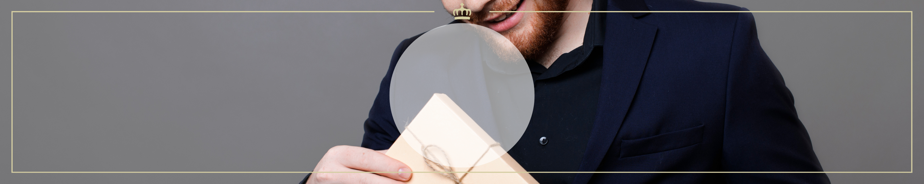 Ein Mann in einem Anzug hält eine Lupe vor eine Geschenkbox und lächelt dabei. Das Bild suggeriert Neugier und Überraschung.