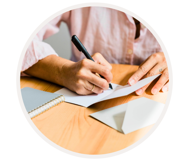 Person in rosafarbenem Hemd schreibt eine Karte und steckt sie in einen Umschlag