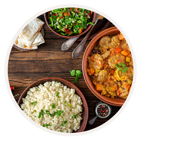 Ein gedeckter Tisch mit Schüsseln voller Couscous, Gemüse und frischem Salat, serviert mit Brot und Pfefferstreuern.