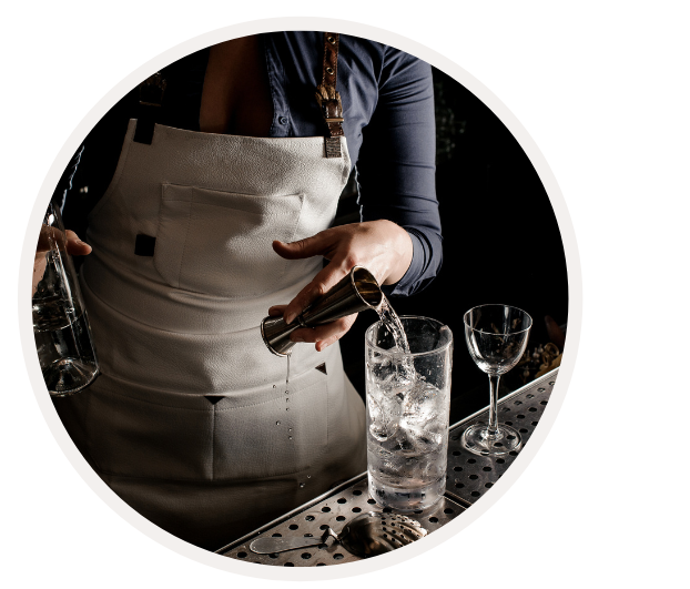 Barkeeper gießt Getränk in ein Glas mit Eiswürfeln neben einem Weinglas an der Bar