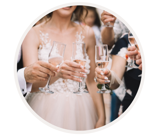 Mehrere Personen halten Champagnergläser in der Hand und stoßen zur Feier einer Hochzeit an. Die Braut trägt ein elegantes, weißes Kleid.