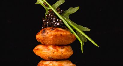 Drei vegetarische Blinis, gestapelt und mit Kaviar sowie einem Rucola-Blatt garniert