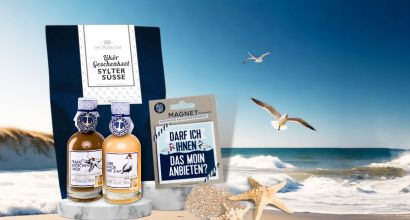 Geschenkset mit zwei Flaschen Sylter Süße Likör und Küstenmagnet auf einem Strandhintergrund mit Möwe und Meer.