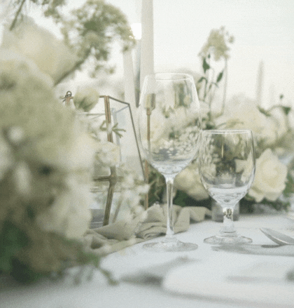 Detailaufnahme eines festlich gedeckten Tischs mit Weingläsern und einem eleganten Blumenarrangement in Weißtönen