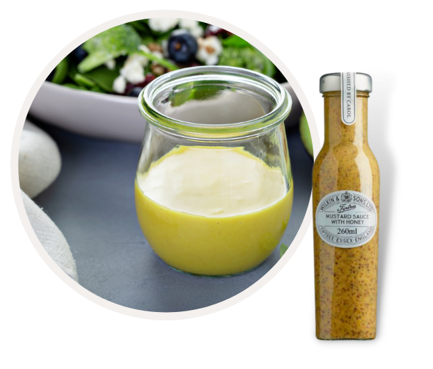 Ein Glas Honig-Senf-Sauce steht neben einem frischen Salat und einer Flasche der Sauce.