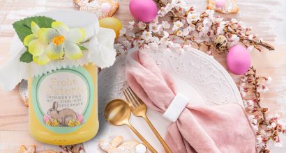 Frühlingshafte Tischdekoration mit rosa Serviette, goldfarbenem Besteck, Ostereiern, Blüten und dekorativem Kerzenglas