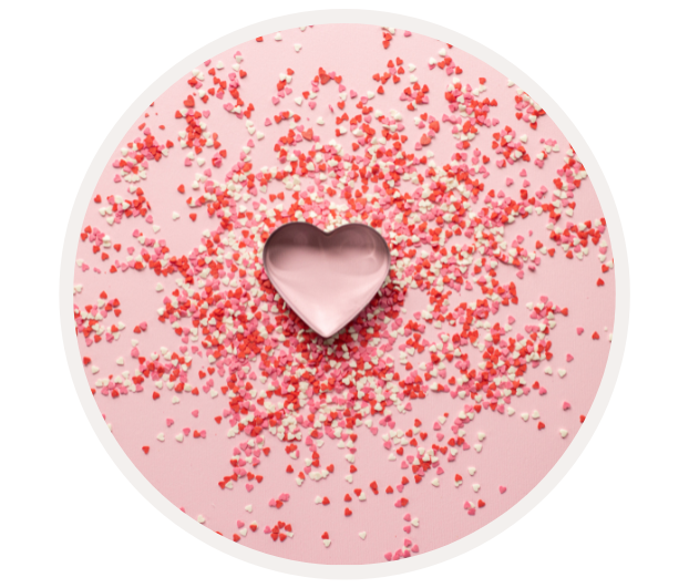 Herzförmige Schüssel mit kleinen, roten und weißen Zuckerstreuseln auf rosa Hintergrund verstreut