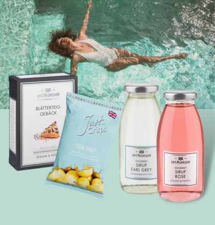 Eine Auswahl an Gourmet-Produkten vor einem Pool-Hintergrund, darunter Blätterteiggebäck, Chips und zwei Sirupe in Flaschen.