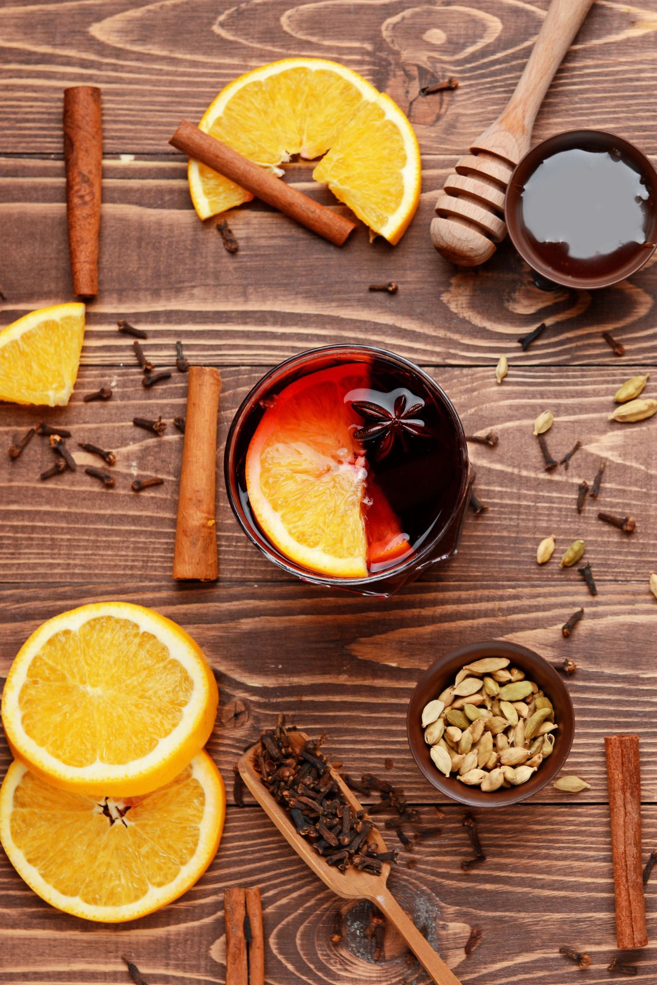 Zutaten für Glühwein: Orangen, Zimtstangen, Nelken, Sternanis, Honig, Kardamom auf Holztisch