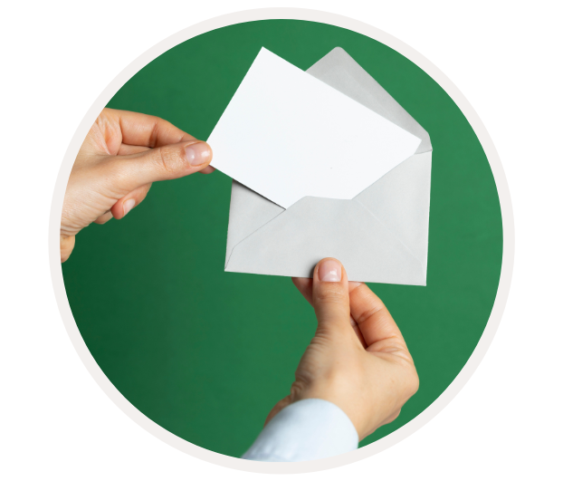 Nahaufnahme einer Hand, die einen grauen Umschlag mit einer leeren, weißen Karte darin vor einem grünen Hintergrund hält.