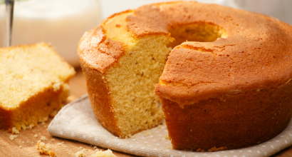 Ein frisch gebackener Rührkuchen mit einem Stück, das auf einem Holzbrett liegt. Daneben steht ein Glas Buttermilch.