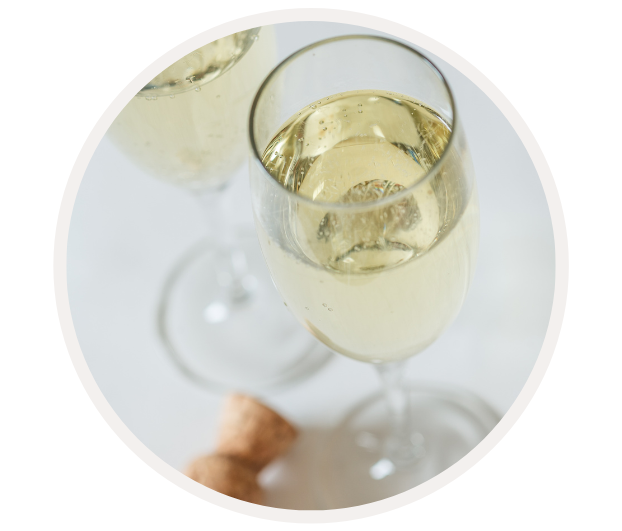 Nahaufnahme von zwei gefüllten Sektgläsern mit einem Korken im Hintergrund